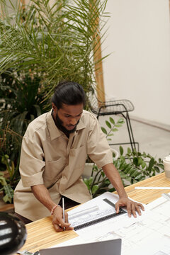 Architect focusing on architectural plans at modern workspace surrounded by indoor plants