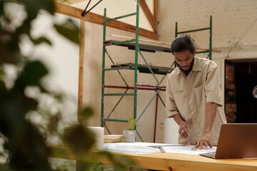 Architect with focused expression analyzing architectural blueprints in workshop setting