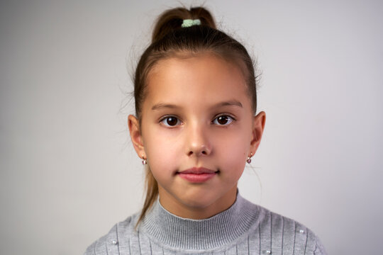 Close-up portrait of a child girl with brown eyes and hairs, looking at camera, white background.