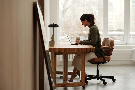 Architect sitting at desk in bright minimalist office, focusing on work with laptop and coffee mug