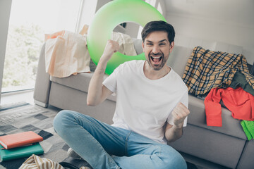 Young man celebrating at home in a casual living room environment, expressing joy and happiness...