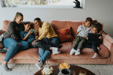 High angle view of multiracial happy family using wireless technologies while sitting on sofa at home