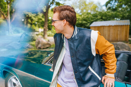 Happy man in letterman jacket leaning on vintage car