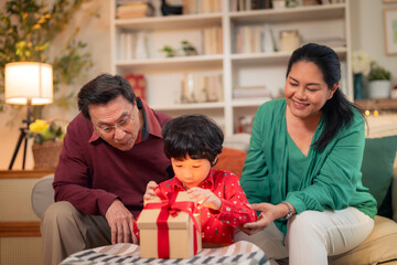 A joyful family moment as child excitedly opens gift with help of grandparents. warm atmosphere highlights love and togetherness during special occasion