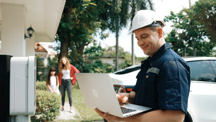 Qualified technician working on home EV charging station installation, making troubleshooting and configuration setup on charging system with laptop for EV at home. Synchronos