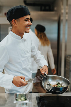 Happy male teenage chef trainee preparing food in saucepan at cooking school