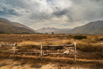 Dirt road with wooden fence at the front to the sandy beach by the mediterranean sea on a beautiful sunny summer day in Sicily