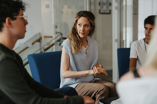 Female mental health professional giving advice to male students while counseling at high school