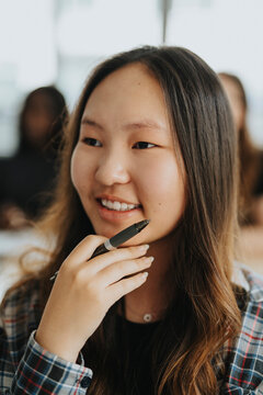 Smiling teenage girl holding pen with hand on chin at high school