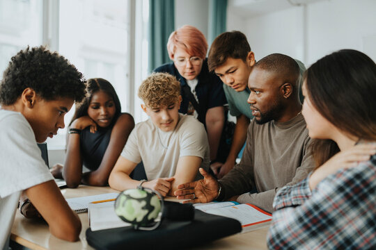 Male teacher gesturing while teaching high school students in classroom