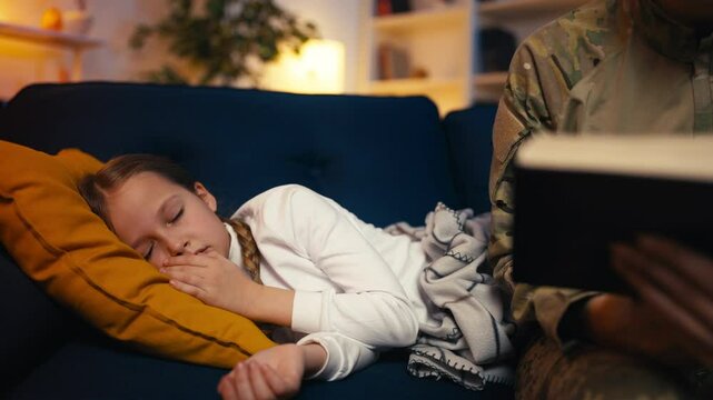 Caring soldier mom reads to sleeping daughter and covers her with a blanket