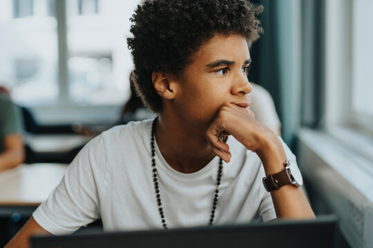 Thoughtful male student with hand on chin in classroom