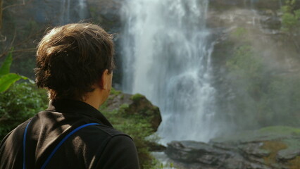 Fototapeta premium Person Admiring Majestic Waterfall in Lush Forest, Nature and Relaxation.