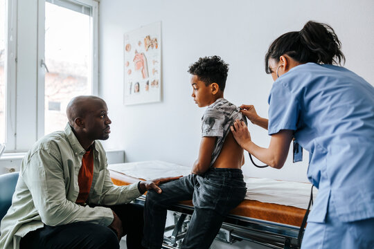 Father sitting by son getting examined by female pediatrician in medical examination room