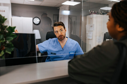 Male receptionist assisting patient standing at hospital