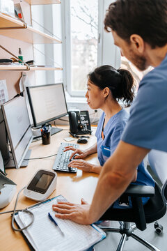 Focused female doctor typing on computer while working with coworker in clinic