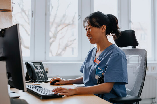 Smiling female healthcare worker working on computer while sitting in examination room at hospital