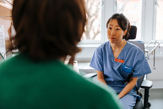 Female healthcare worker talking with senior patient while sitting in examination room