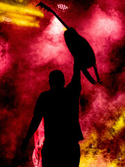 Frontman raising guitar at concert with red and yellow smoke