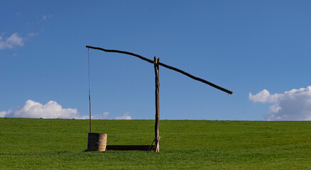 Wooden sweep well on a farm with green grass and blue sky