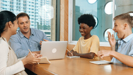 Smart girl ask teacher a question while show idea while diverse student working classwork. Group of multicultural children pointing at notebook while happy boy sharing idea at classroom. Edification.