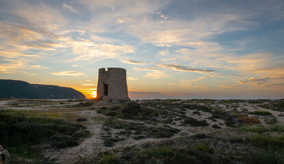 Obraz premium An old stone windmill on a beach at sunset with stunning sunlight and sky clouds.