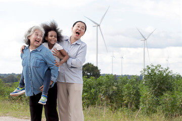 Grandma piggybacking cute granddaughter girl at wind turbine farm. Asian elderly and aunty play...