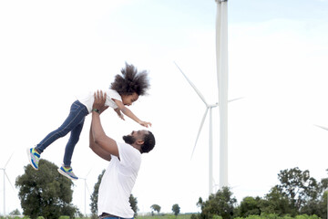 Happy African family spend time together at wind turbine windmill farm. Father play with curly hair...