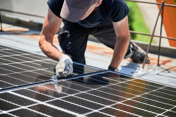 Worker building photovoltaic solar panel system on rooftop of house. Close up of man engineer in...