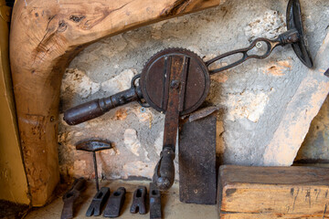 A vintage wheel brace hand drill, a bradawl, and hammer heads on a shelf.