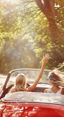 Two girls traveling by car, waving to people, rear view. Outdoor road trip photography