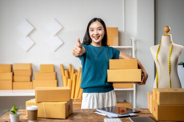 Asian sme business owner holding parcel showing thumb up in warehouse