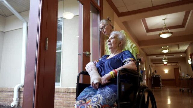 Closeup of elderly woman with cast on broken arm and black eye hematoma in wheelchair with woman family member talking to her.