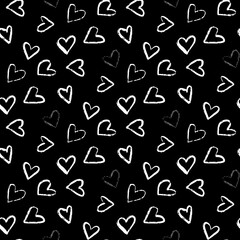 A seamless pattern of various hand-drawn white hearts tossed on a black background