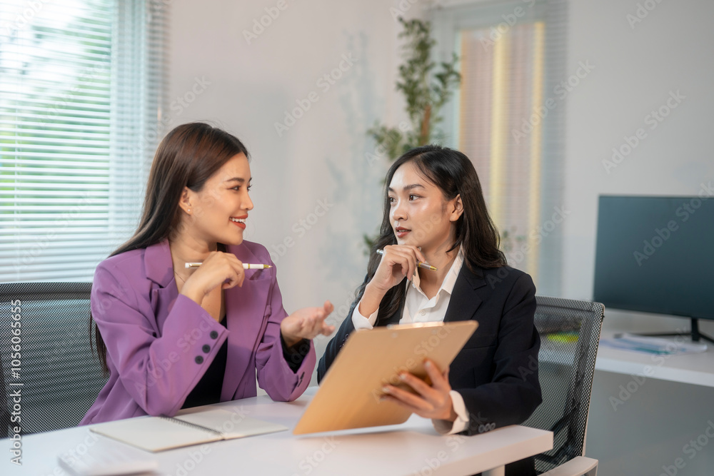 Wall mural two women are sitting at a desk, one of them holding a clipboard