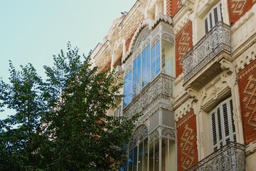 Obraz premium Vintage balconies curvy iron railing painted in white colour on the old-fashioned facade seen through vivid greenery downtown Madrid, Spain