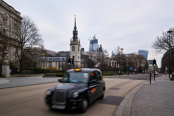 London taxi in motion blur with the city skyline behind driving on a street