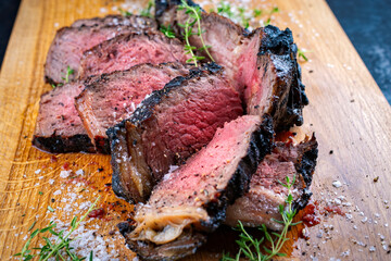Traditional grilled barbecue dry aged tomahawk beef steak meat with salt and fresh herbs served and sliced as close-up on a wooden design board