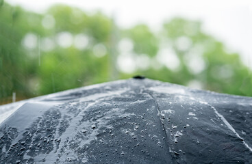Macro of rain water drops falling and splashing on black umbrella while raining outside.
