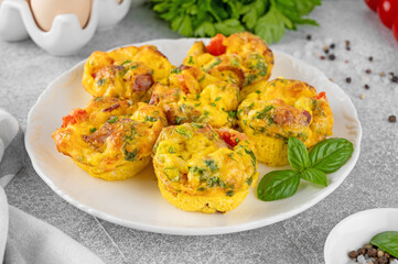 Egg muffins or egg bites with bacon, cheese, vegetables and herbs on a white plate on a concrete background. Healthy breakfast.