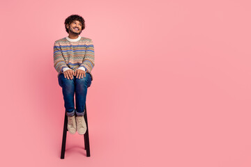 Full body portrait of nice young man sit stool look empty space wear sweater isolated on pink color...
