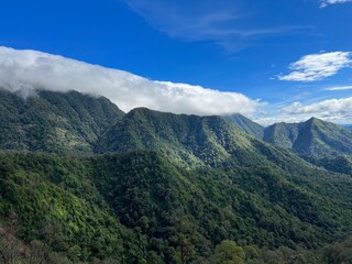 Fototapeta premium Lush green mountains rise under a blue sky, accentuated by white clouds, showcasing the beauty of nature and tranquility