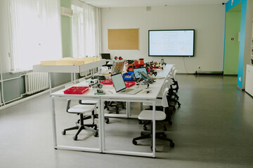 Empty classroom equipped with tables with electronic devices and robots, interactive whiteboard on wall
