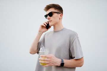 A young man enjoying a refreshing drink while engaging in a phone conversation on a sunny day