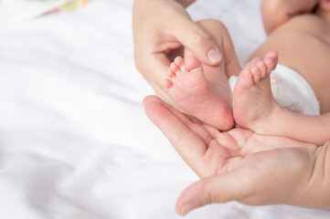A nurturing parent gently holds their newborn's tiny feet, showcasing the warmth and affection shared in this intimate moment, surrounded by soft fabrics and tranquility.