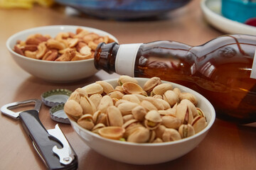 Plates with pistachios and nuts on a table with a beer bottle and a bottle opener, beer snacks, bar...