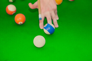 Hand with a cue makes a “bridge” to hit the ball with the cue on the billiard table, the technique of playing billiards, the game of eight-ball.