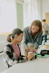 Obraz premium Vertical shot of young female teacher helping with robot wires while student holding robot carefully