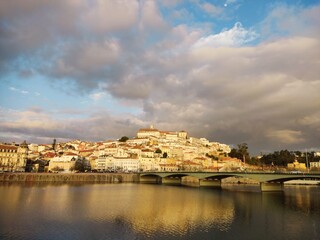 Fototapeta premium This image captures a scenic view of a historical city built on a hillside, likely Coimbra, Portugal, during a picturesque moment with the late afternoon or early evening sunlight