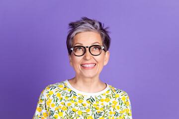 Cheerful woman with glasses smiling against a vibrant purple backdrop in floral shirt